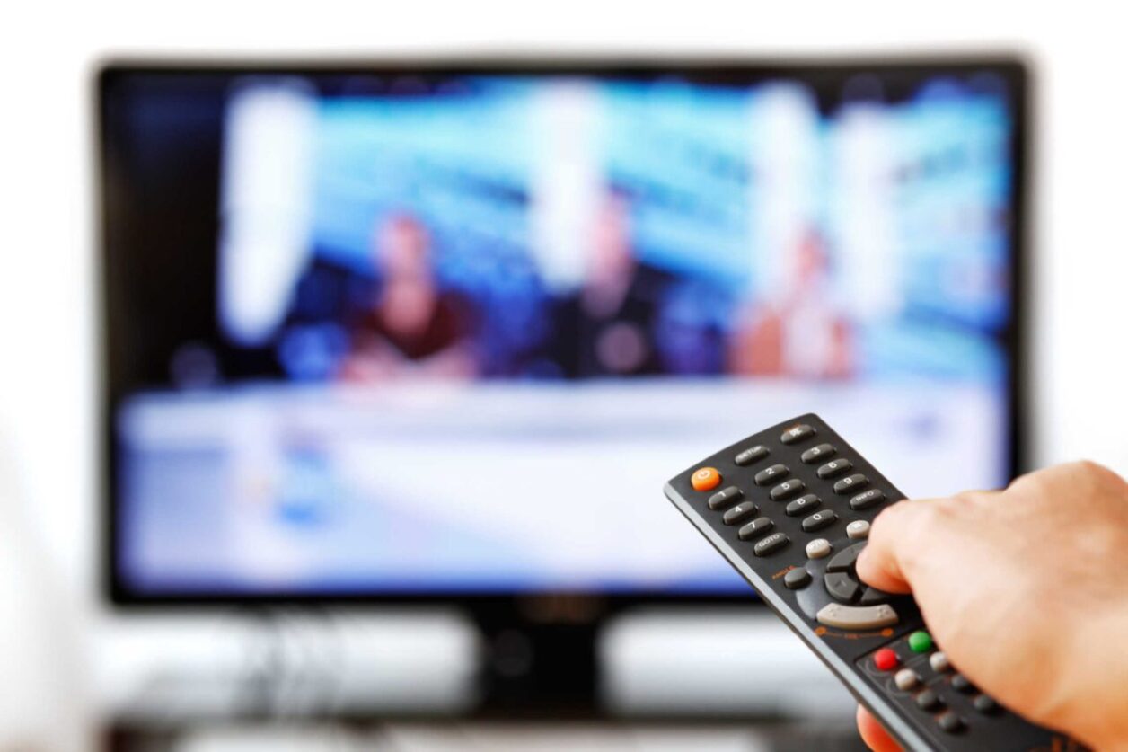 Out of focus TV LCD set and remote control in man's hand isolated over a white background.