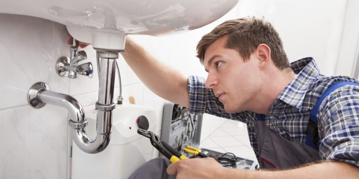 Young plumber fixing a sink in bathroom